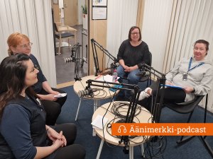 Neljä ihmistä istuu mikrofonien äärellä äänittämässä podcastia.