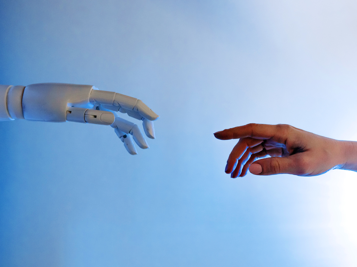 Robottikäsi ja ihmisen käsi ojentuvat toisiaan kohden.